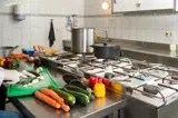Iemand die met beschermende handschoenen groenten bereidt in een keuken.